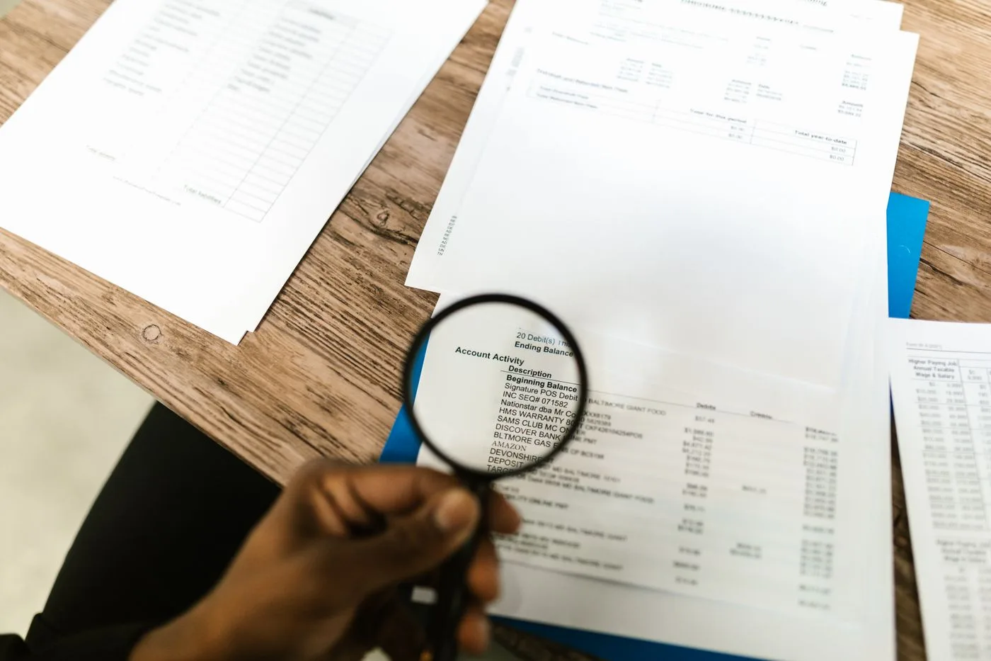 Close-up of hand using magnifying glass to review documents.