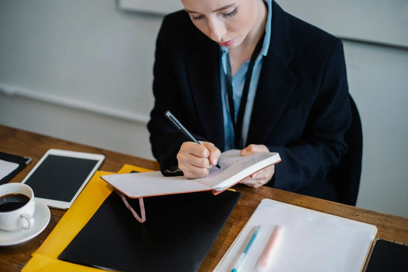 High angle of crop female in formal wear sitting at table and writing notes in planner during work day