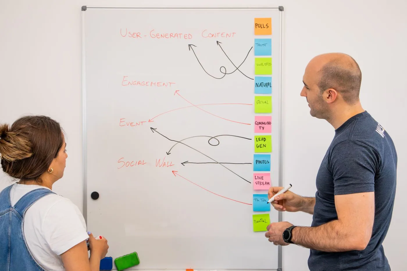 Two colleagues brainstorm ideas on a whiteboard during a creative strategy session