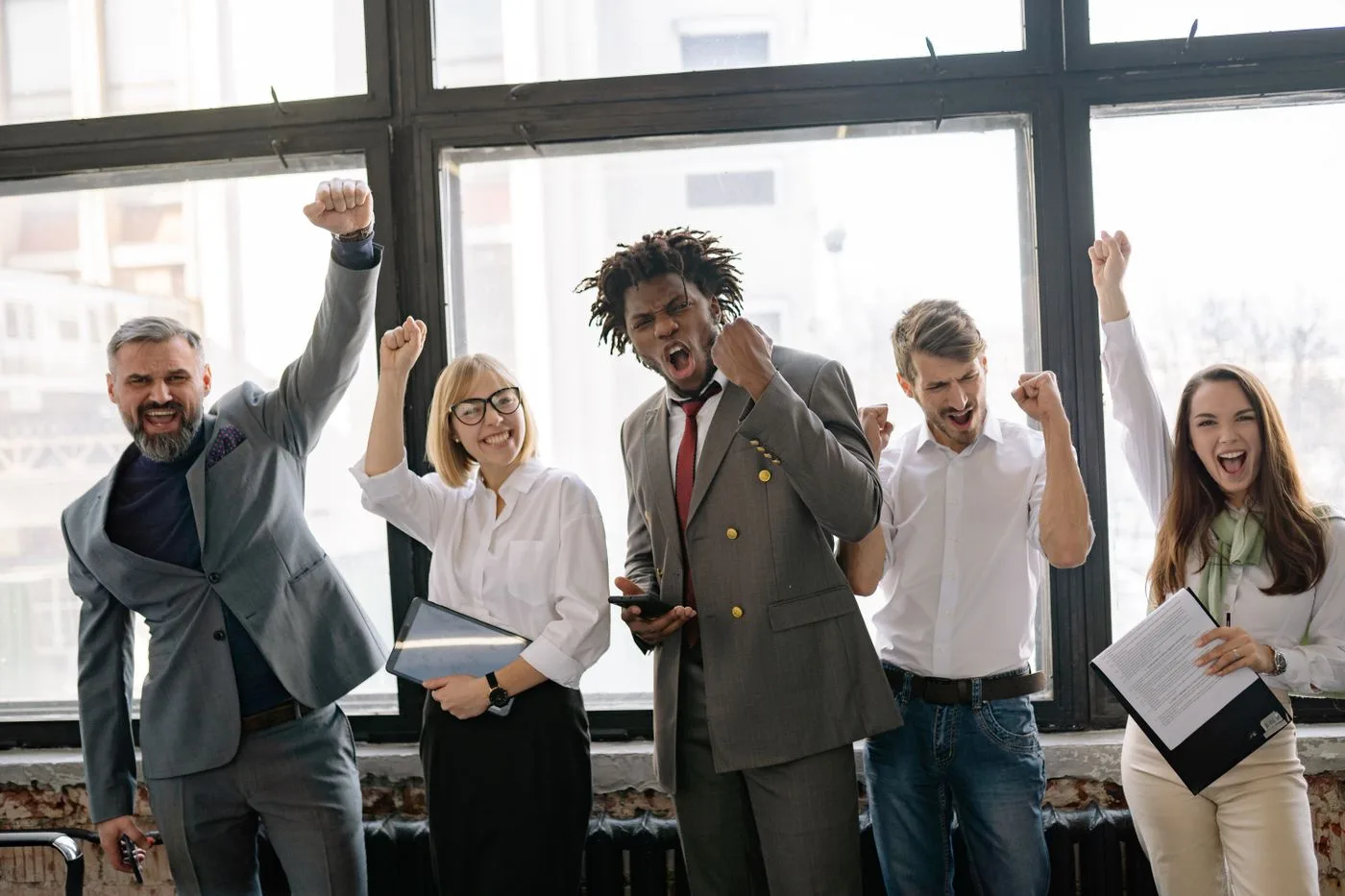 Group of diverse professionals celebrating achievement in office setting with enthusiasm