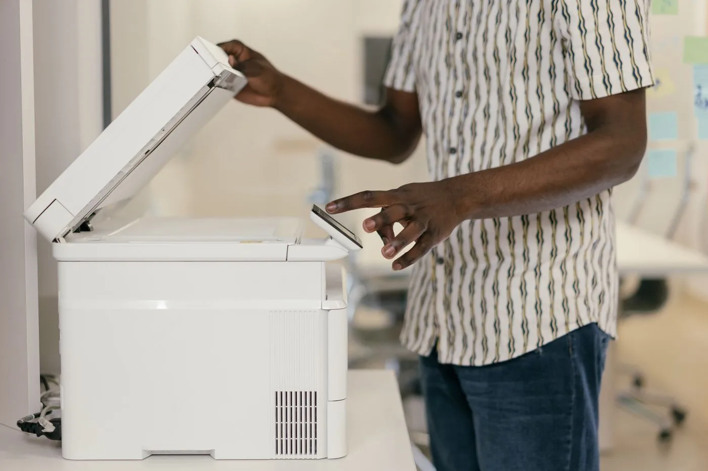 Person operating photocopier in modern office setting, engaging with technology