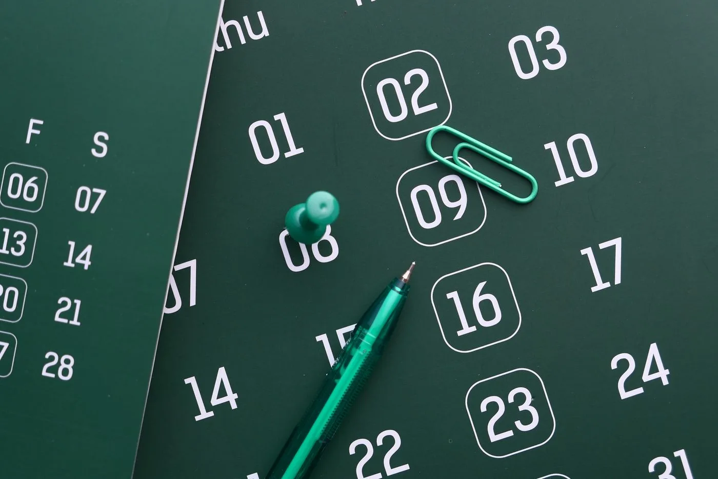 Close-up of a green calendar with pen, push pin, and paper clip for planning and organization
