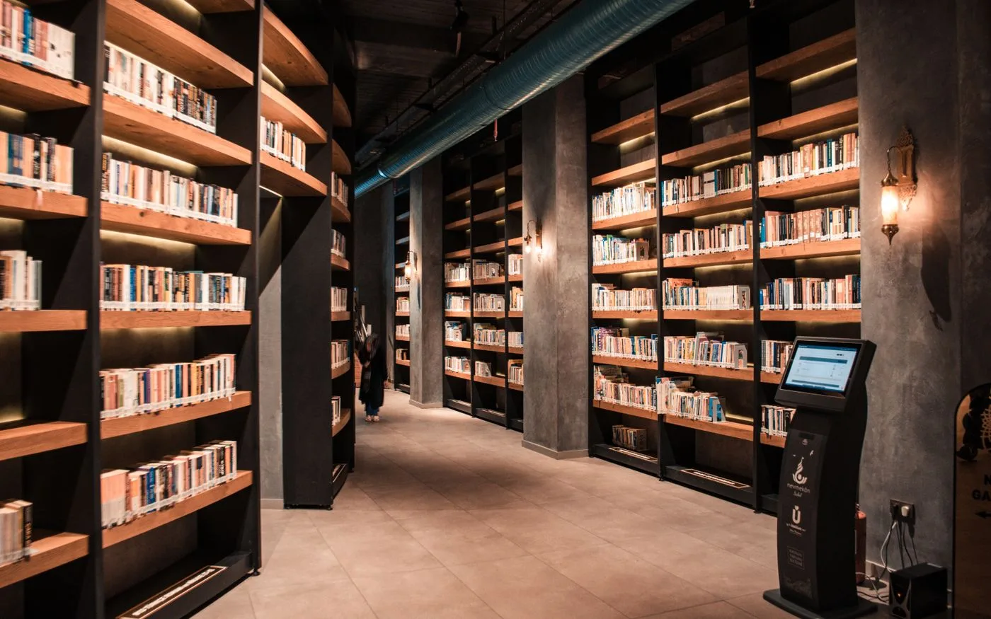 A spacious library featuring tall wooden bookshelves filled with books and ambient lighting