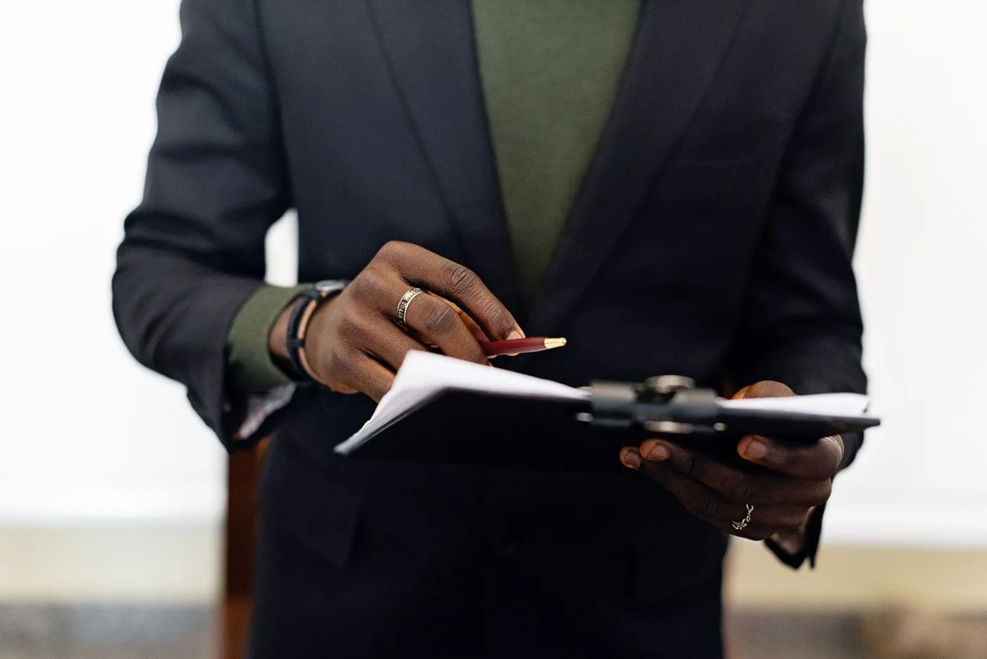 Close-up of an adult in a blazer holding a clipboard with documents and a pen indoors