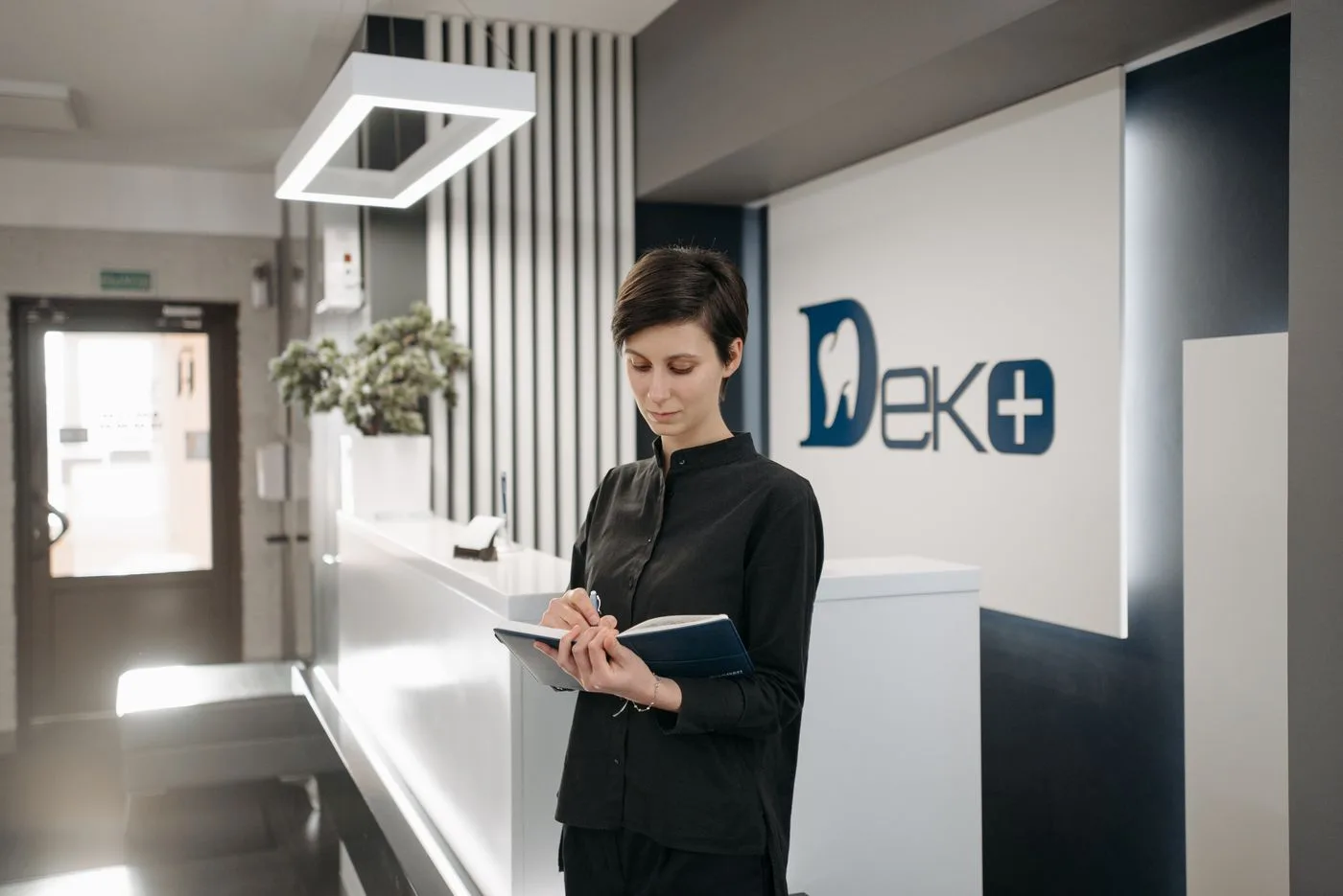 Female receptionist writing notes at dental office reception. Professional healthcare setting