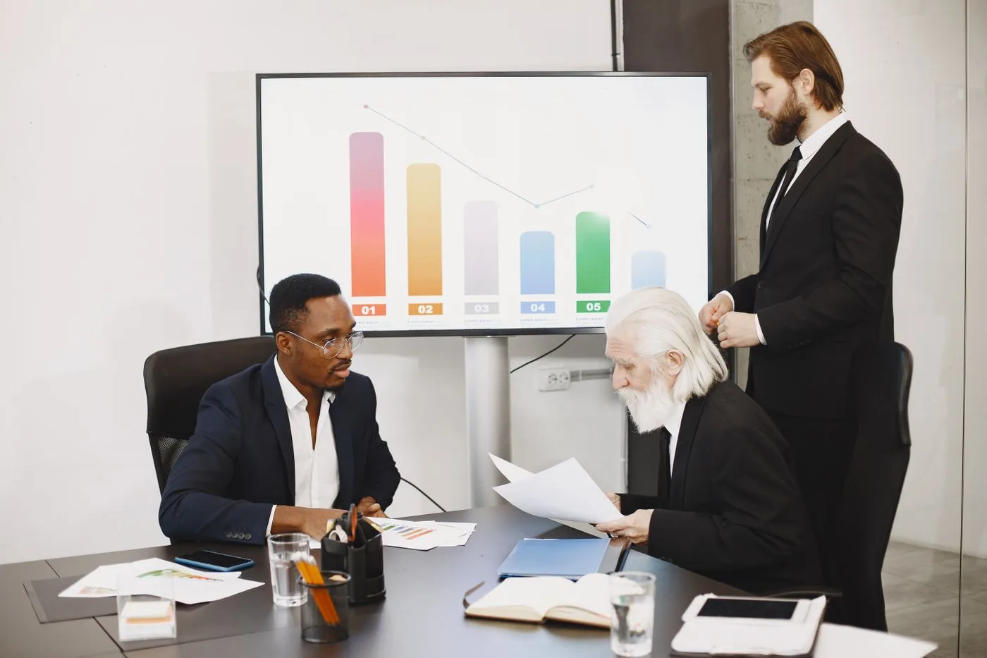 Three businessmen discussing financial data in a modern office setting with charts