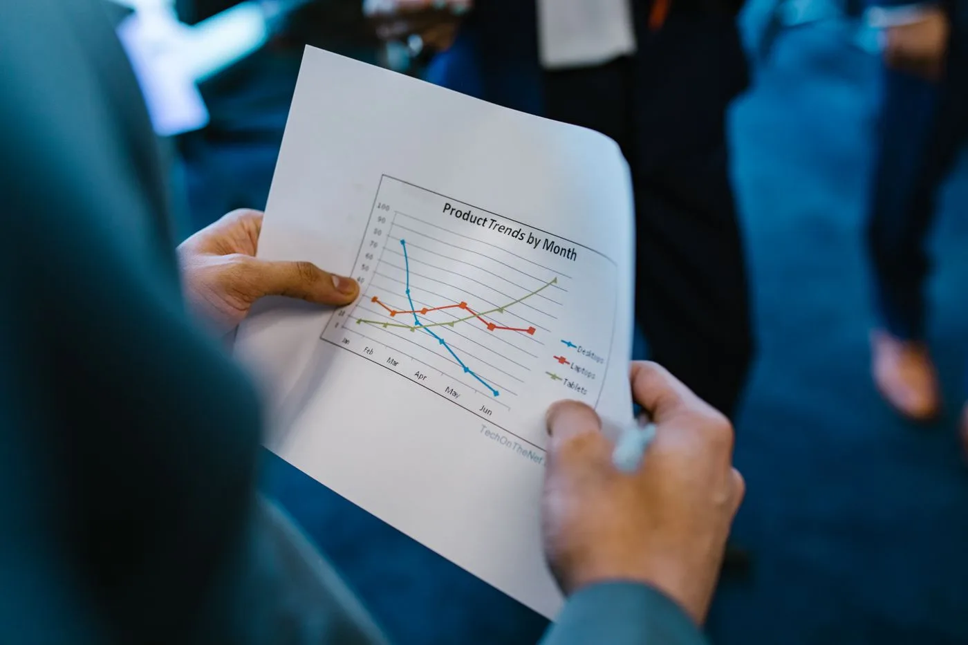 Close-up of hands holding a paper with a line graph showing product trends by month during a business meeting