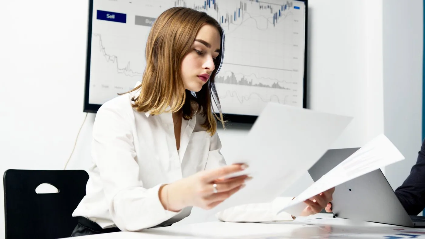 Focused woman analyzing financial reports in a modern office setting with charts and graphs