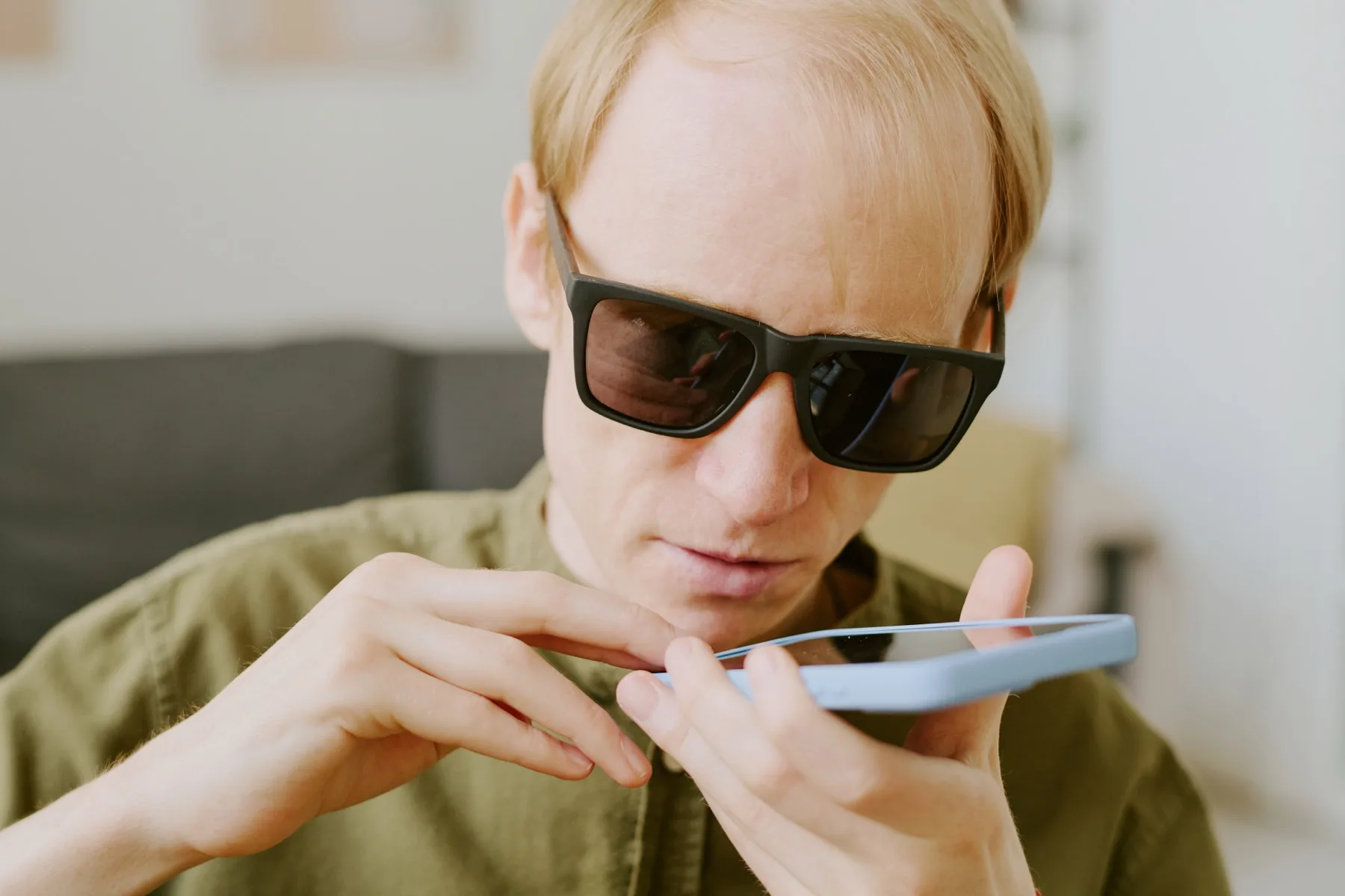 Man in dark glasses holding a smartphone flat and speaking into it