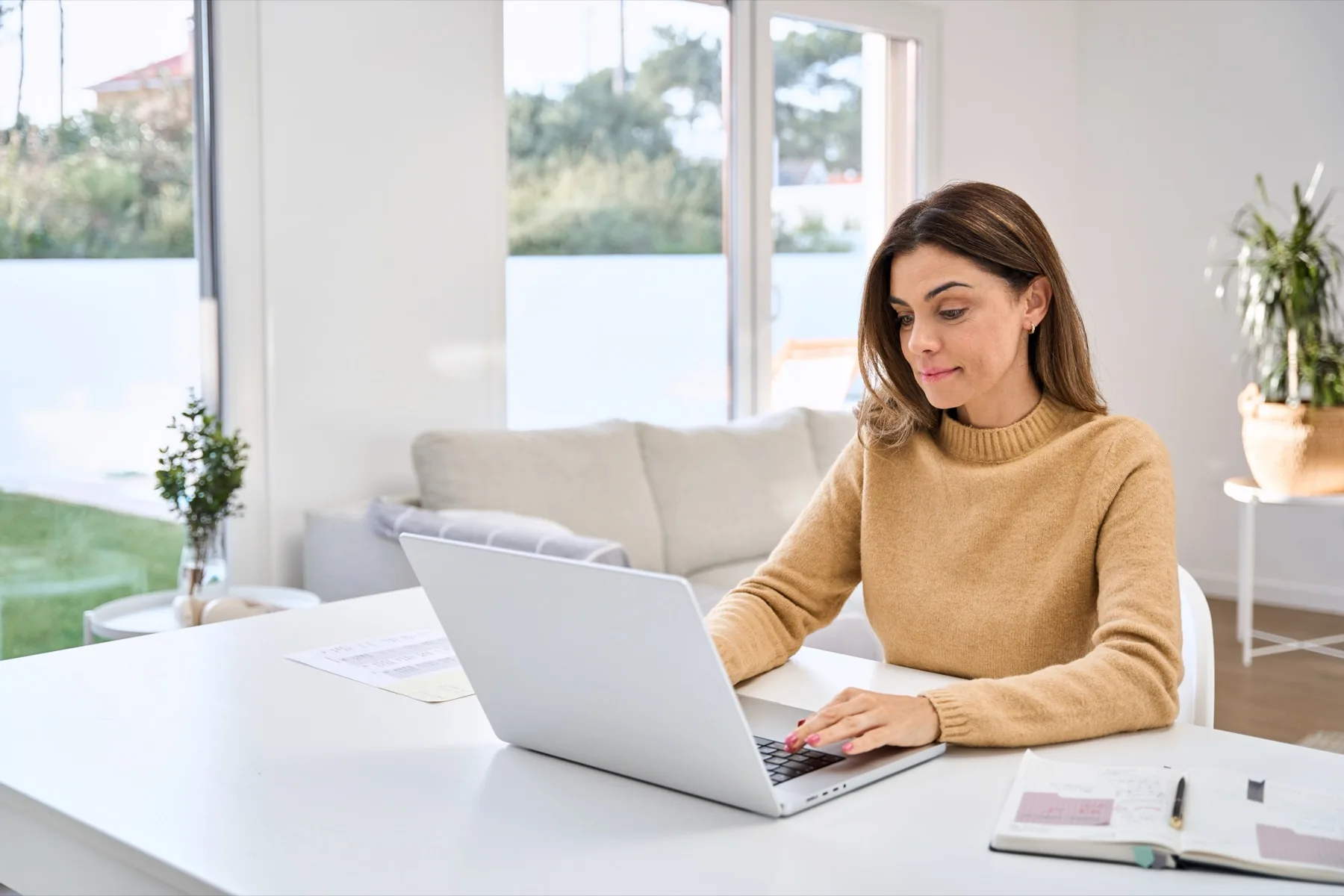 Woman drafting copy on a laptop at a bright home office desk
