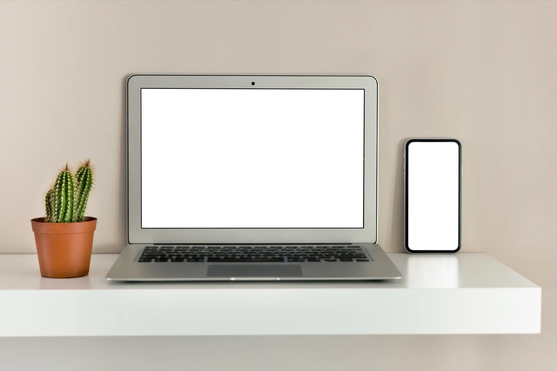 Laptop and smartphone side by side on a white shelf, the two screens a caption has to work on
