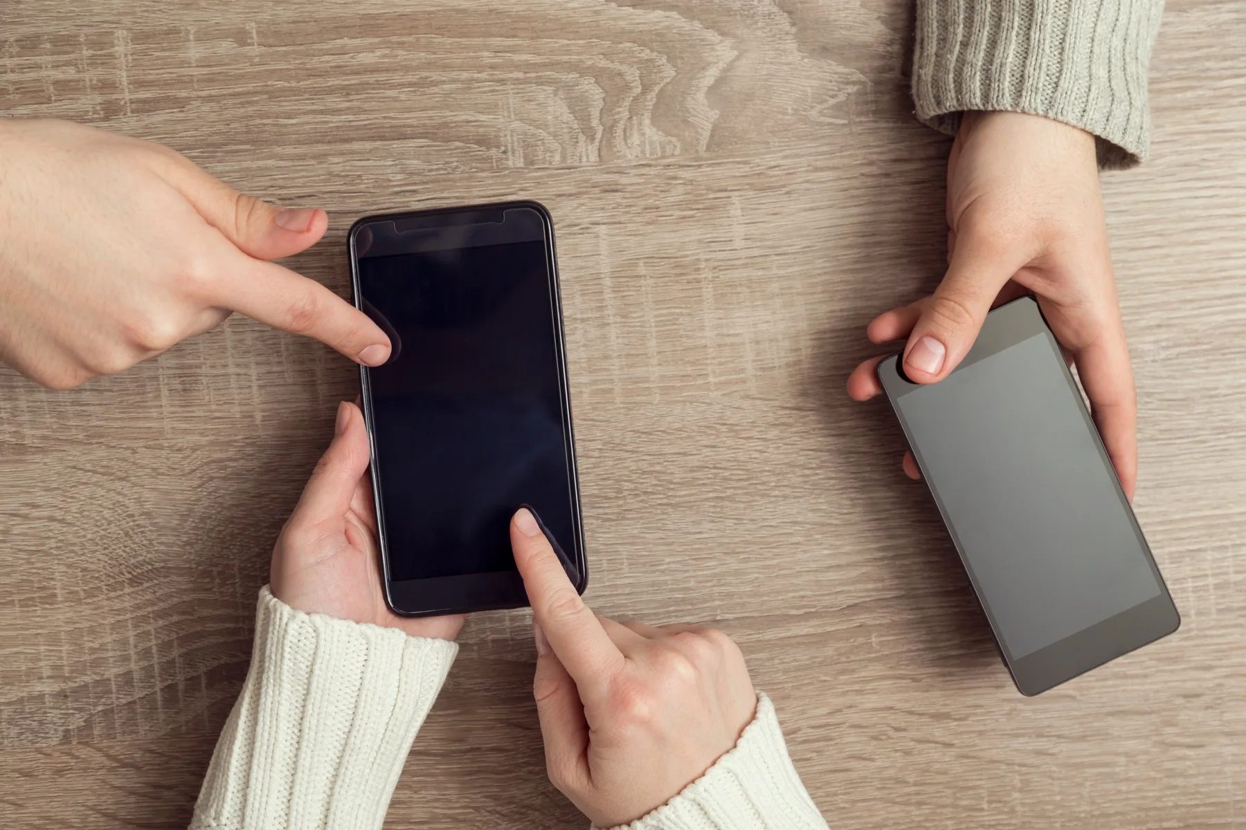 Two people comparing posts on their smartphones across a wooden table