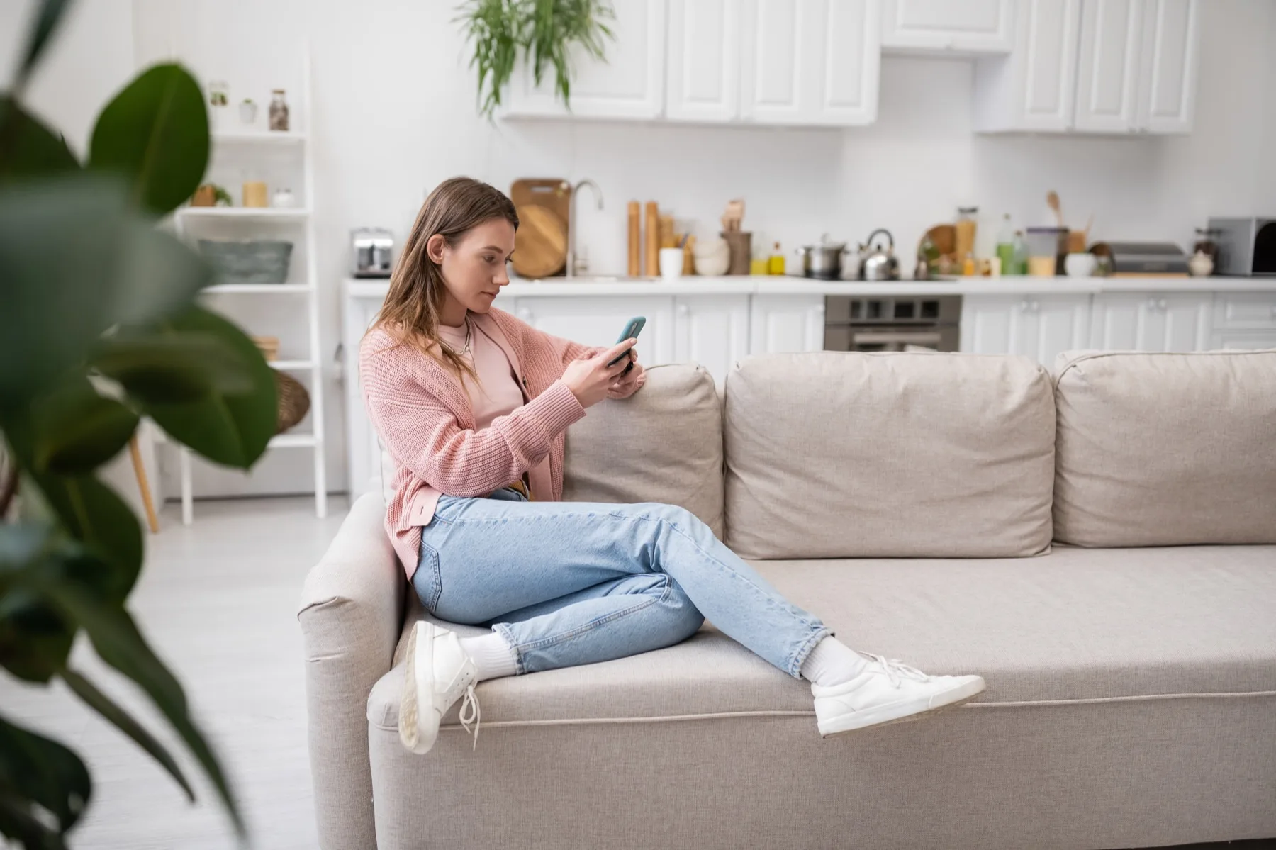 Woman relaxing on a sofa in a bright living room, reading her social media feed on her phone