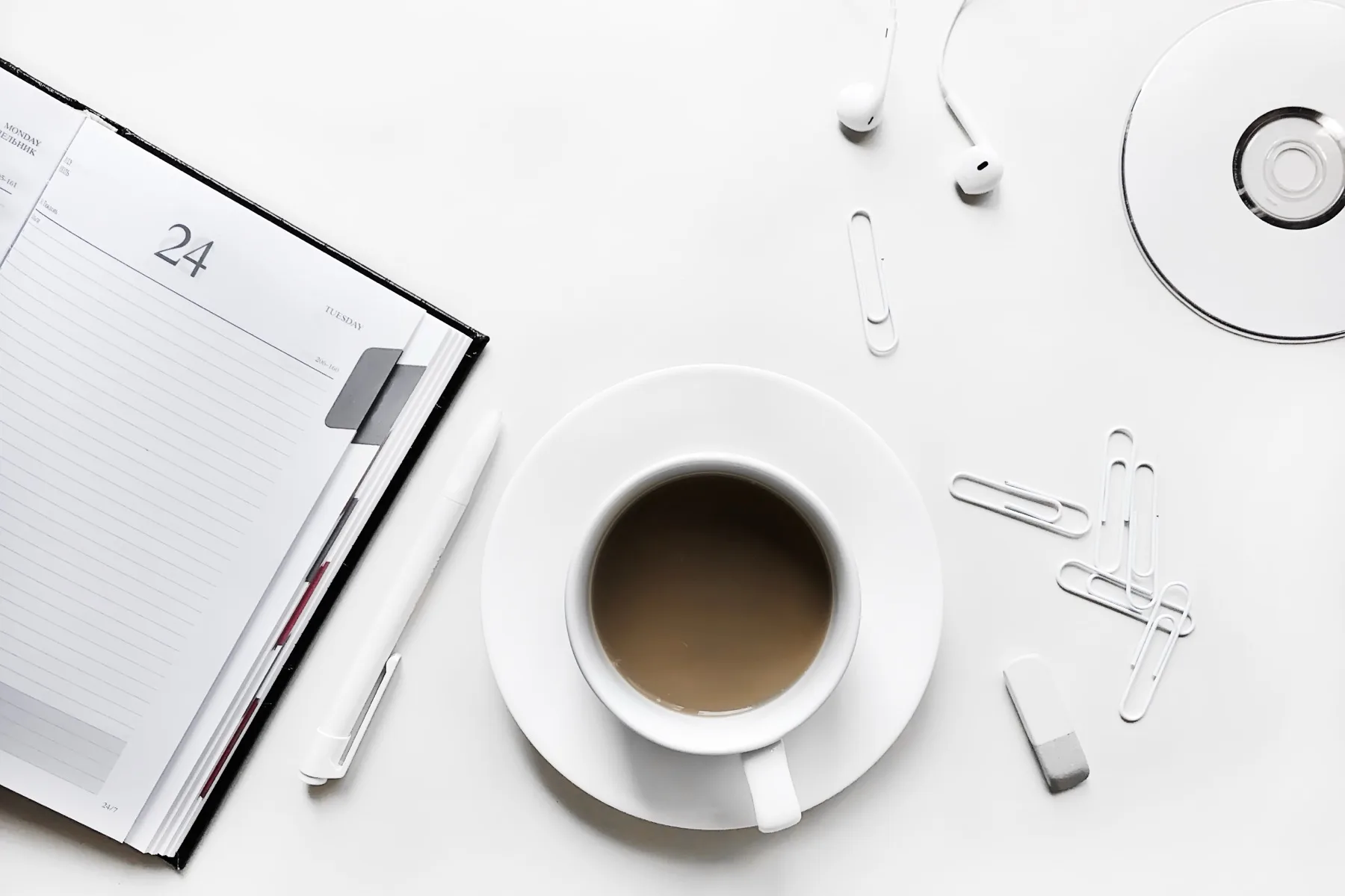 Overhead flat lay of a weekly planner, a cup of coffee and earphones on a white desk