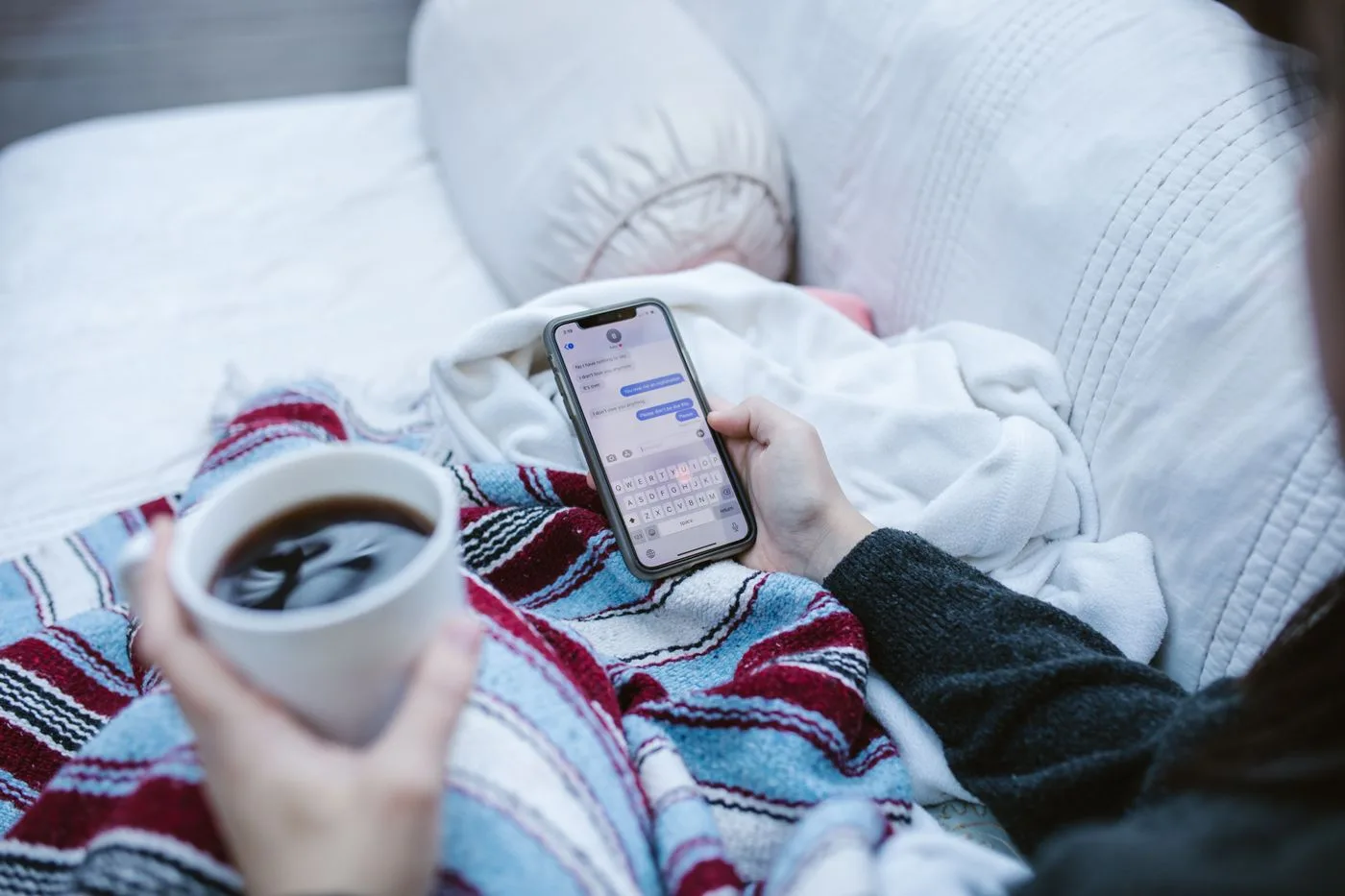 Person relaxing indoors with coffee and smartphone, texting in a cozy setting