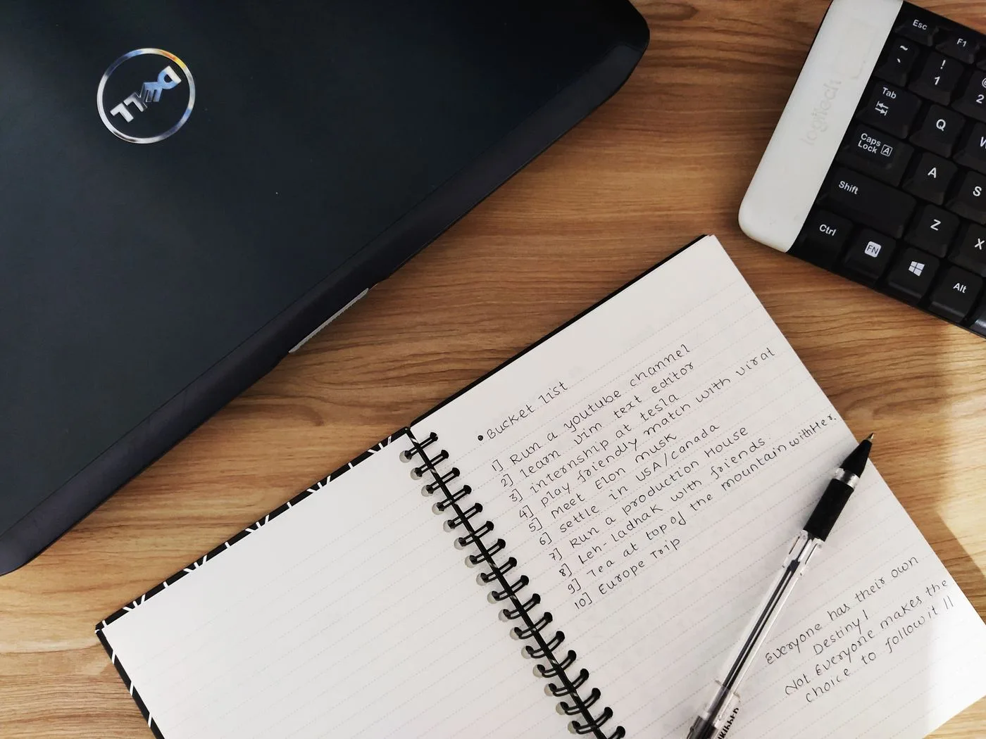 Flat lay of a workspace featuring a laptop, notebook, and keyboard on a wooden desk