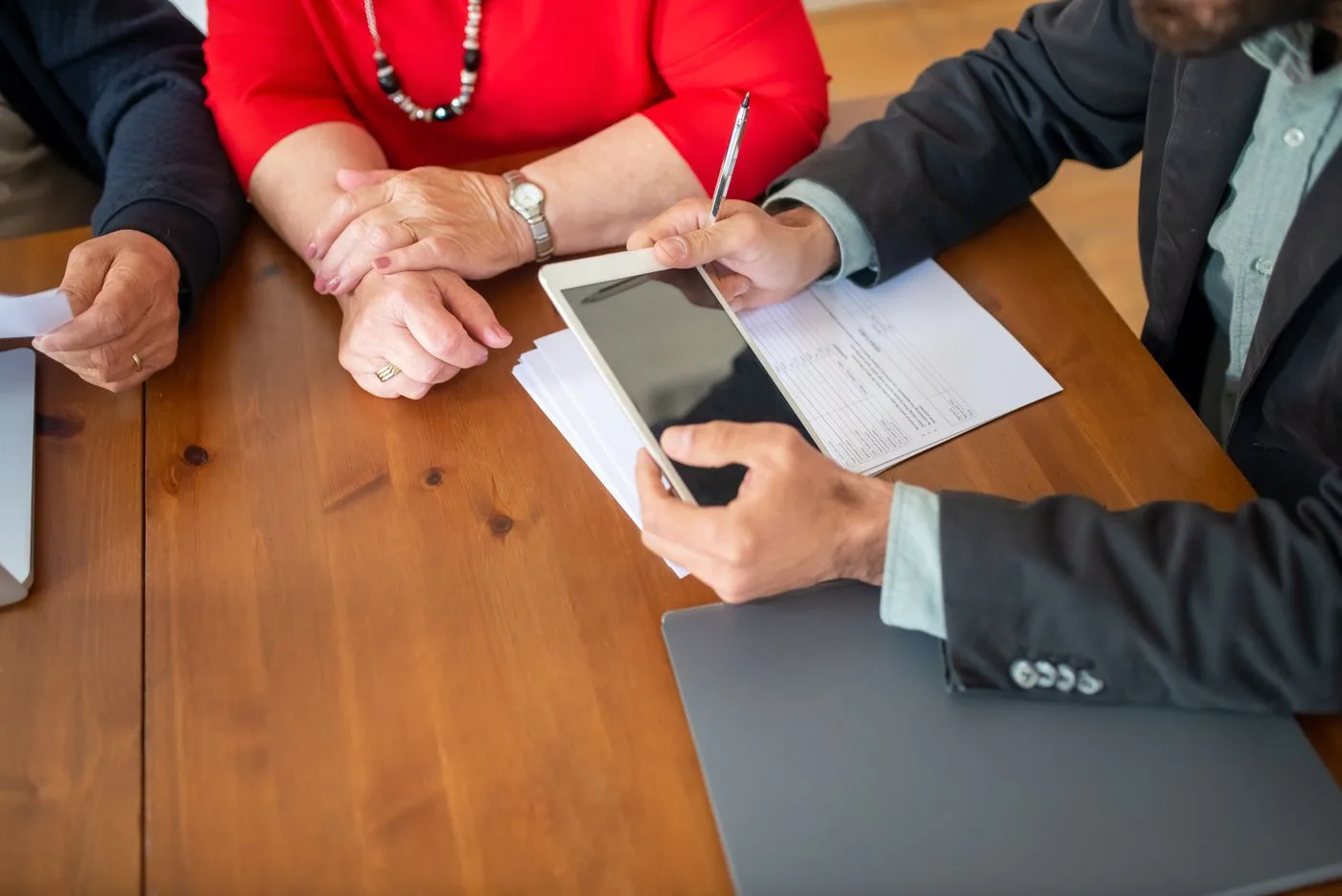Business meeting at a wooden table with consultant reviewing documents and using a digital tablet