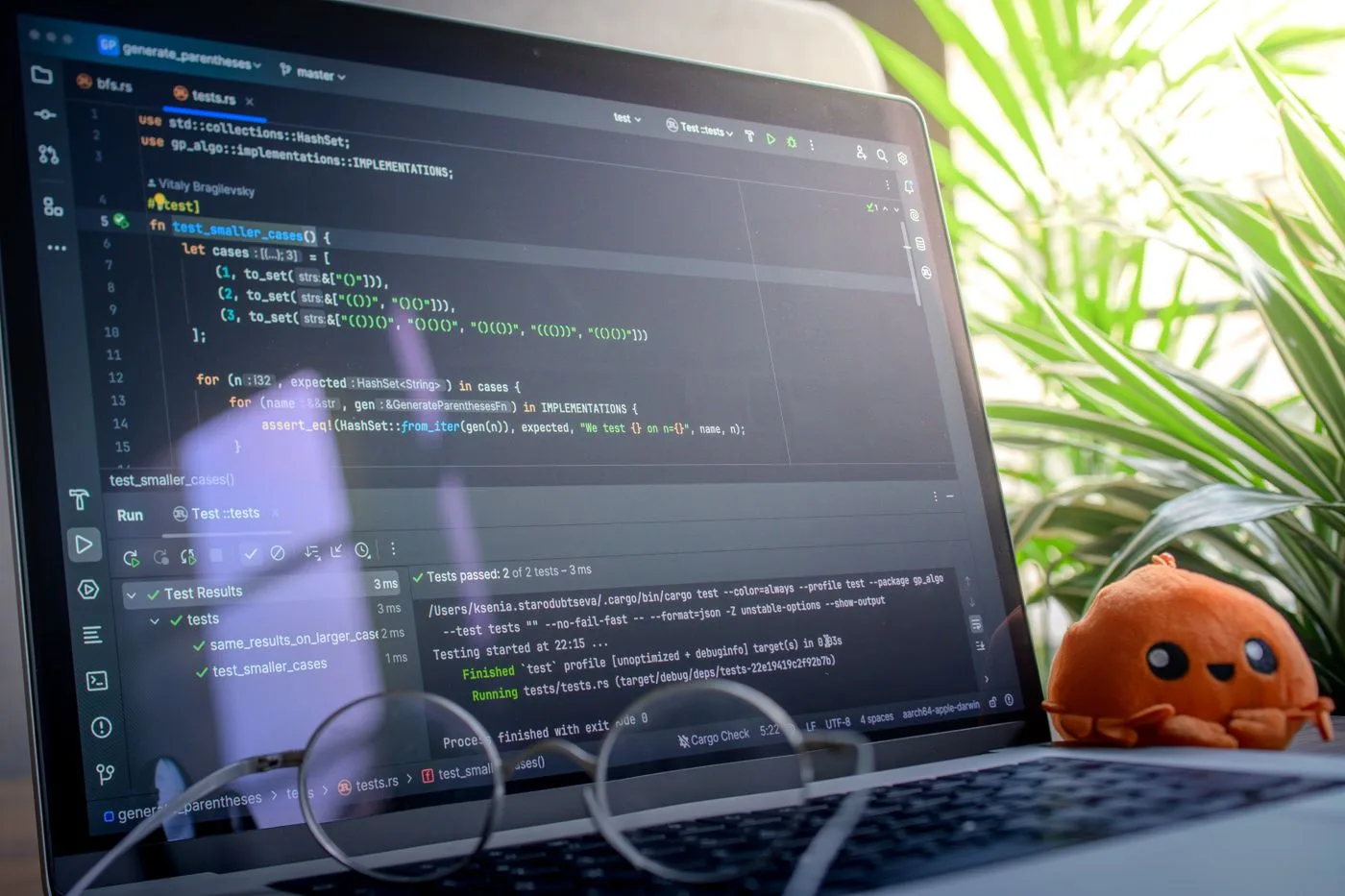 Open laptop displaying code next to a plush toy, set in a bright room with plants
