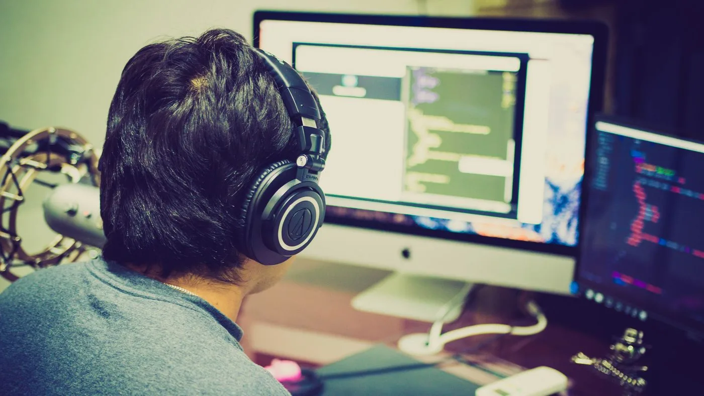 A programmer with headphones focuses on coding at a computer setup with dual monitors