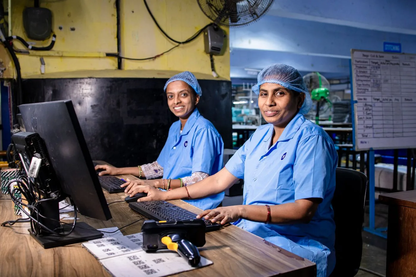 Two female workers at a textile factory operating computers in an industrial setting