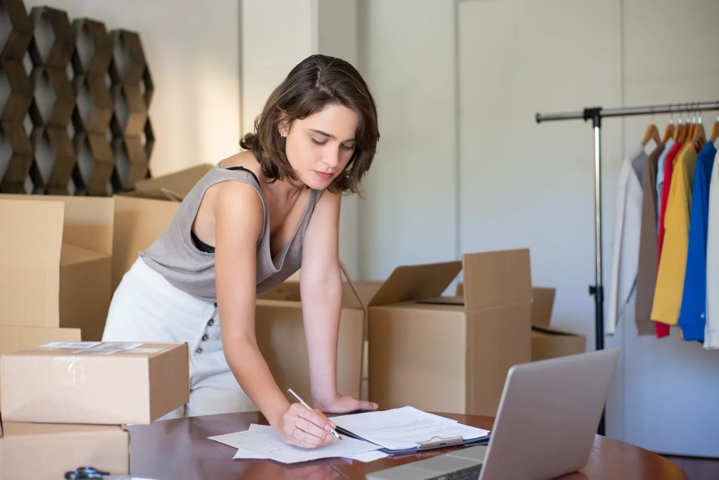 Young woman managing her online clothing business from home office with boxes and laptop