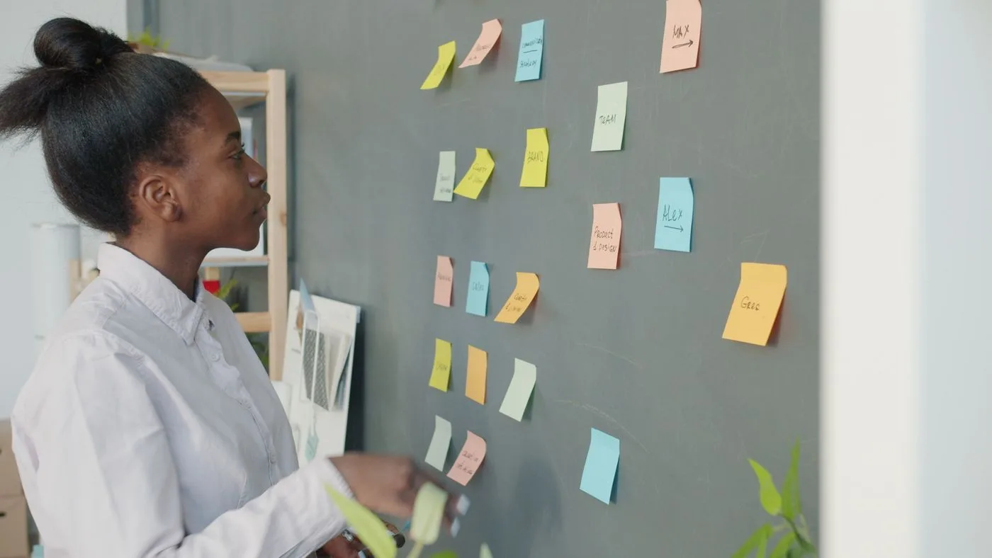 Focused young woman analyzing sticky notes on a chalkboard for project planning