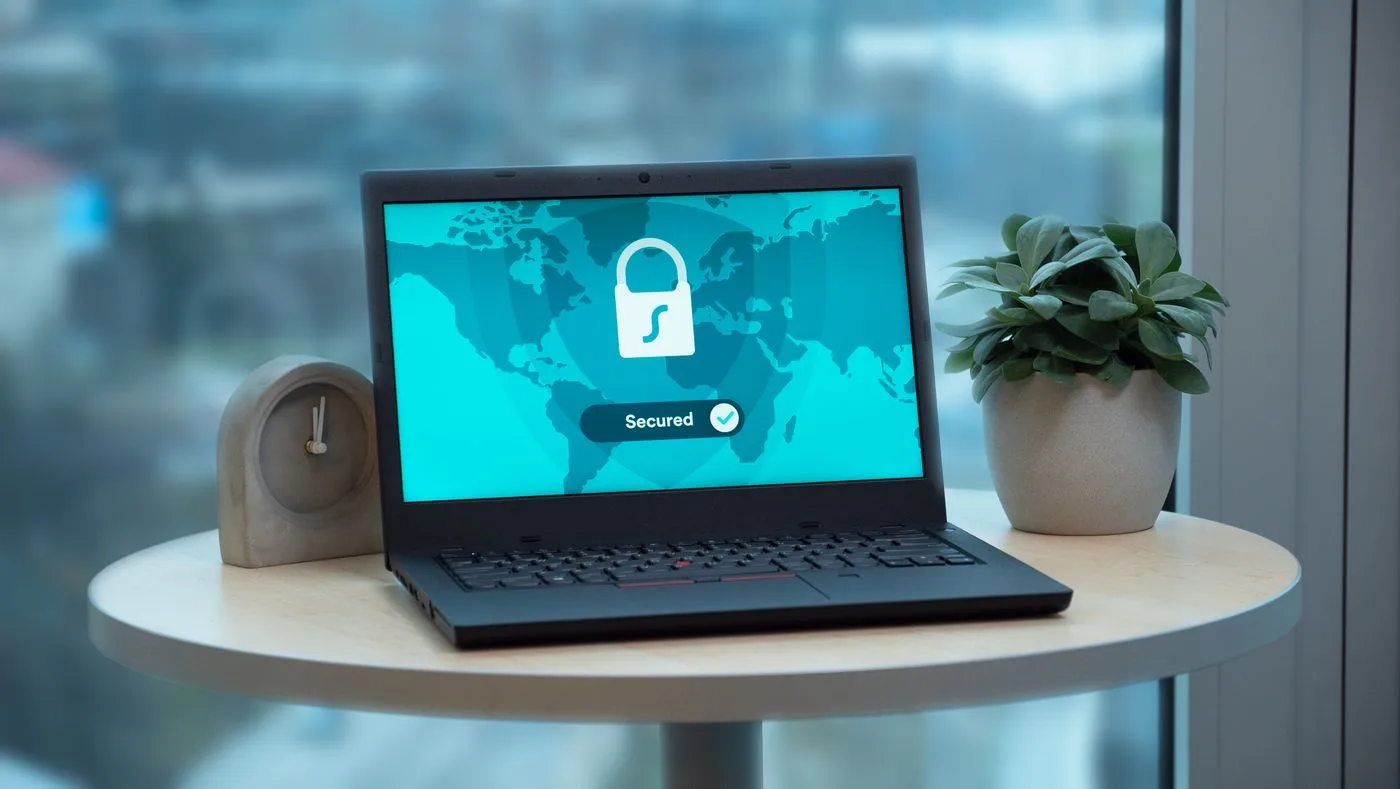 Laptop displaying a security lock icon on a table with a potted plant and clock