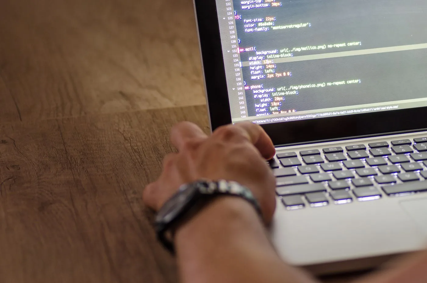 A developer's hand interacting with code on a laptop screen in a workspace setting