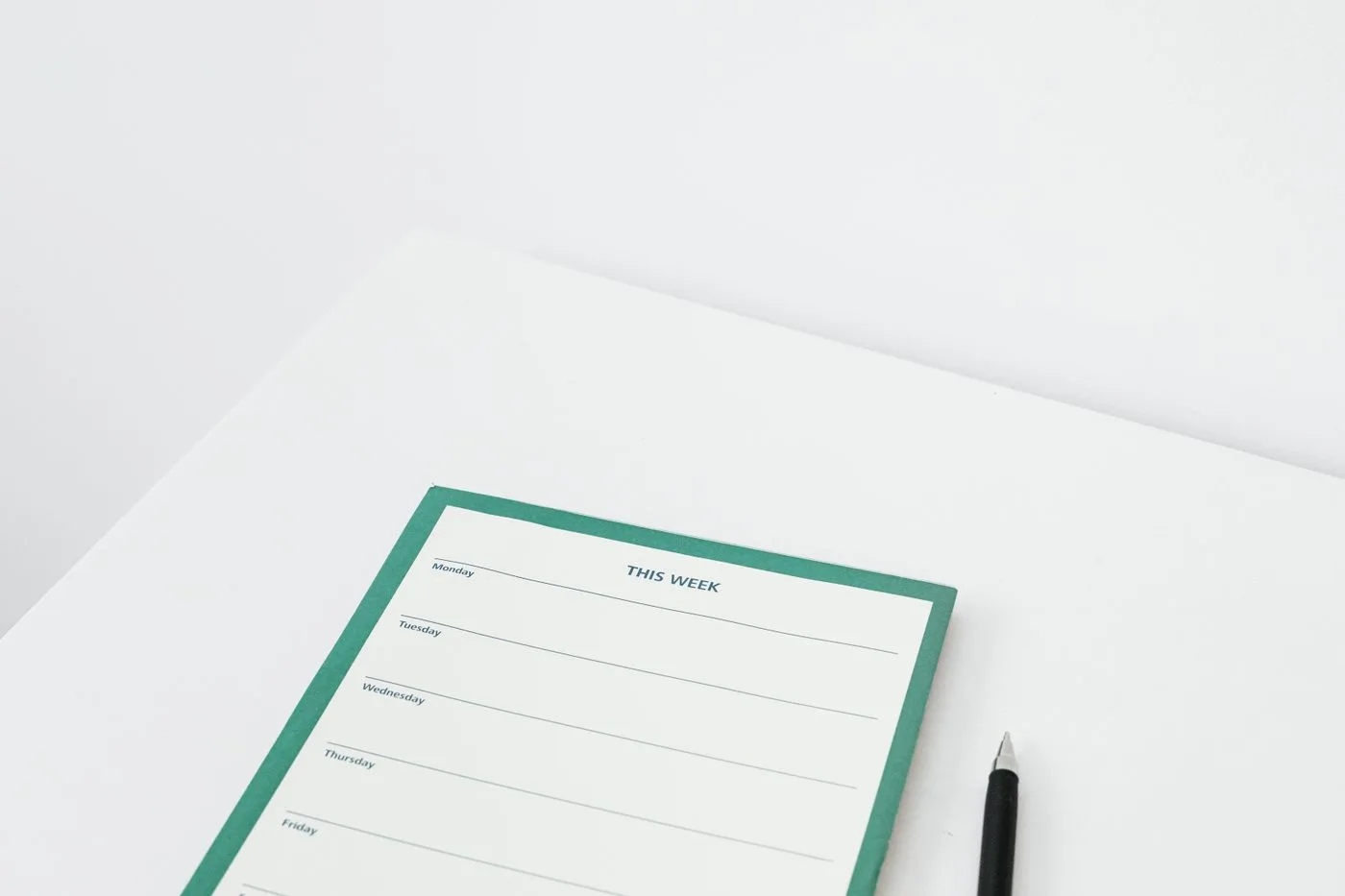 A clean and minimalist weekly planner with a pen on a white desk