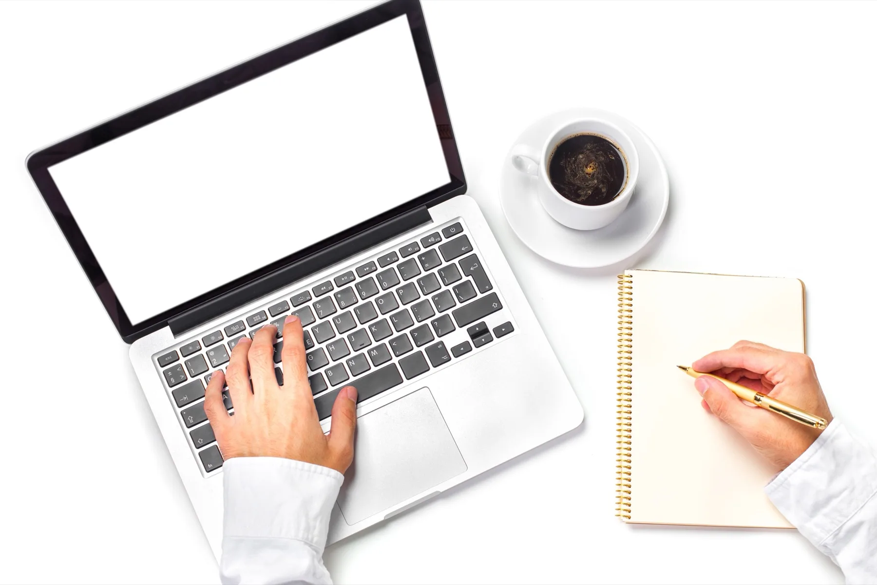 Hands typing on a laptop beside a notebook and a cup of coffee, seen from above
