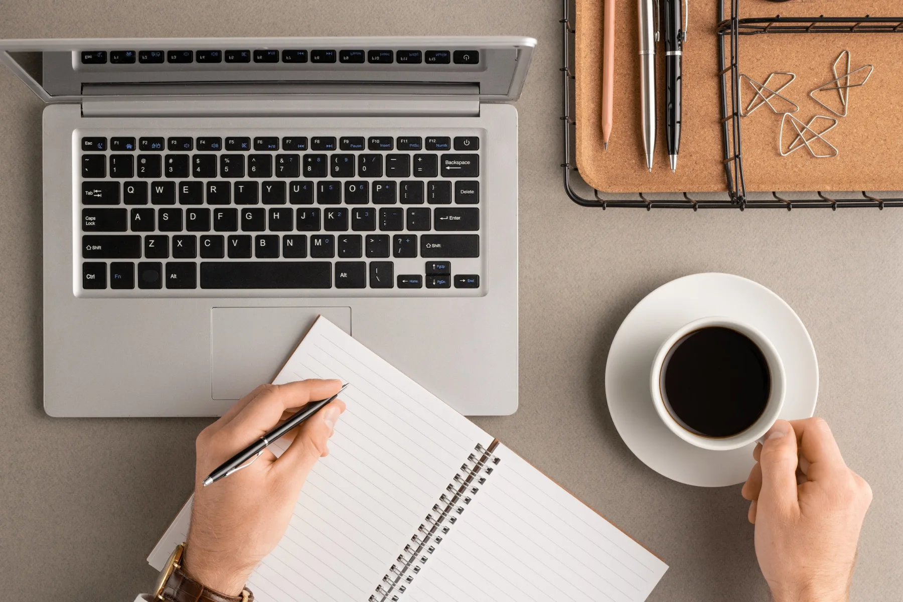 Hands taking notes beside a laptop and a cup of coffee