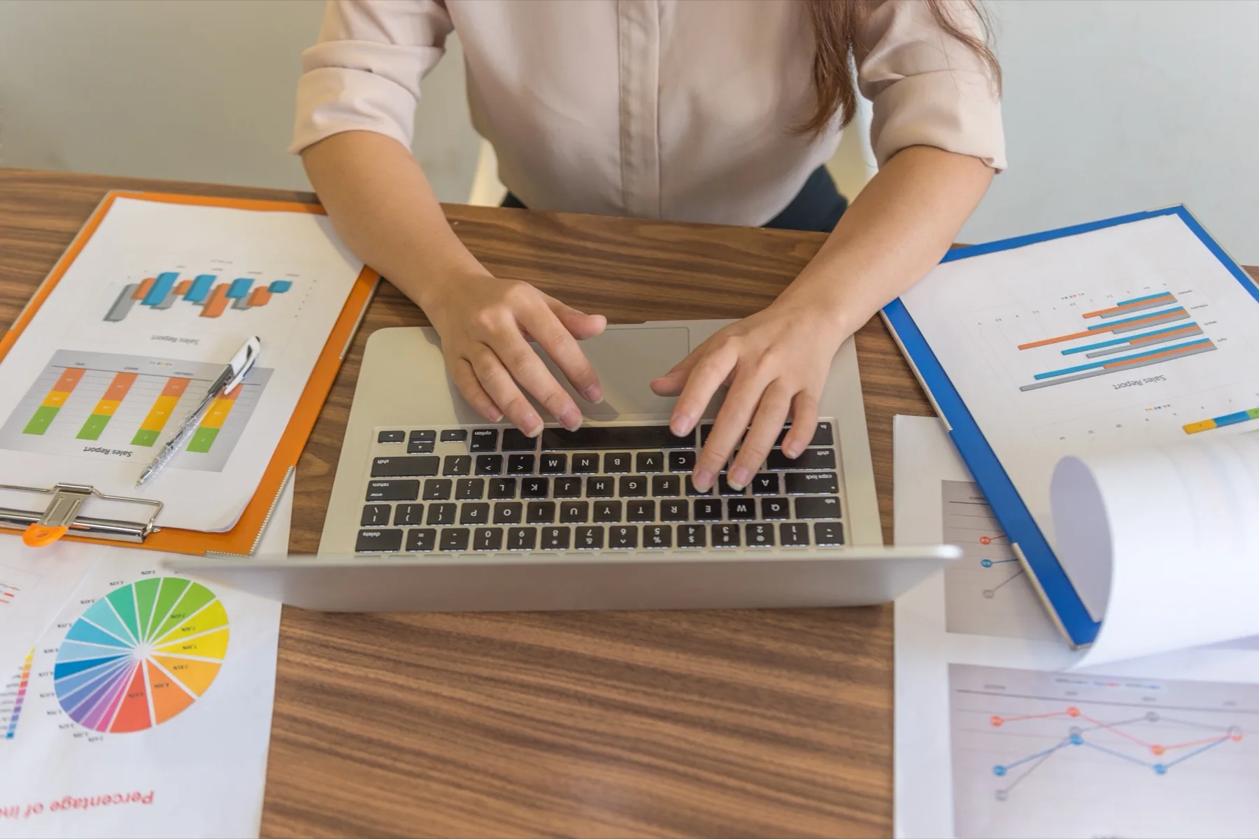 Overhead view of hands typing on a laptop surrounded by printed charts