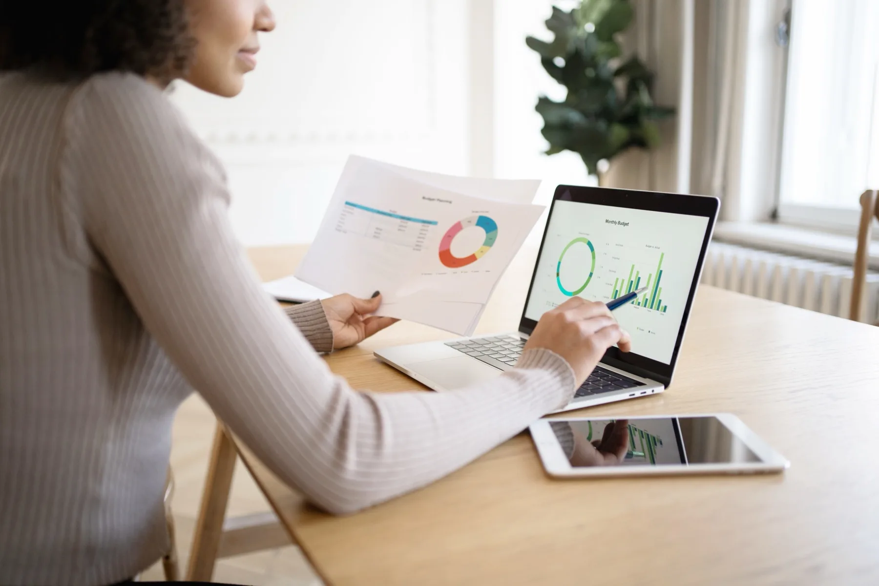Woman comparing charts on a laptop and tablet at a desk