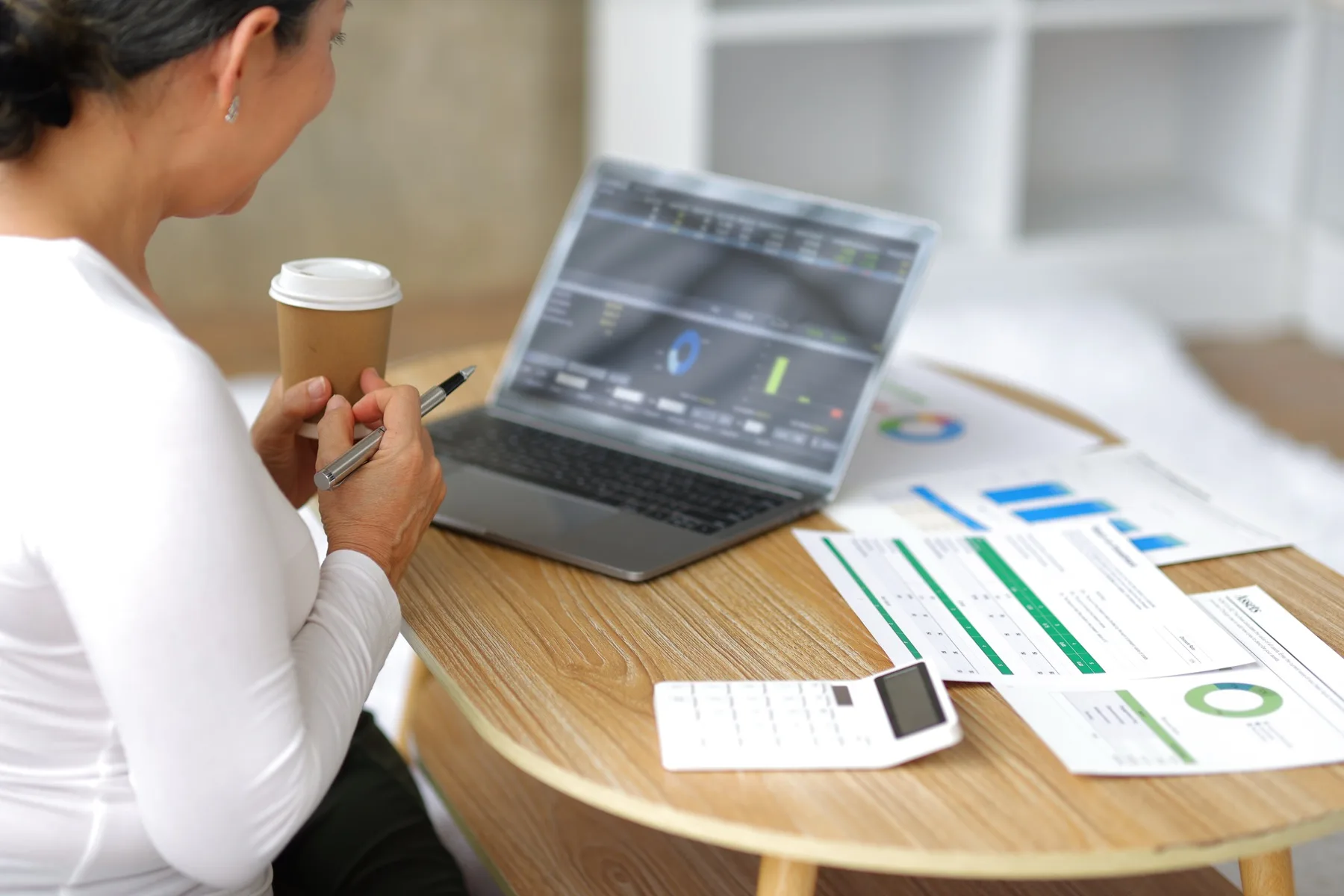 Woman reviewing printed charts beside a laptop and coffee