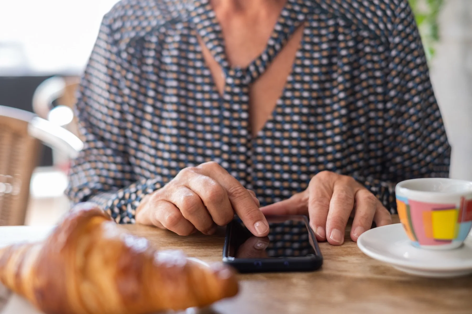 Customer using a phone at a cafe table with coffee and a croissant