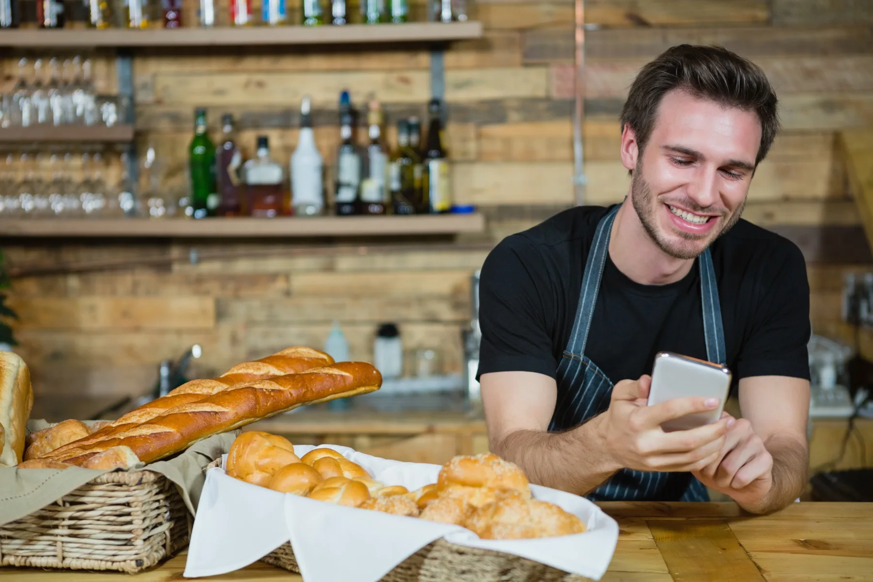 Smiling baker using his phone at the bakery counter
