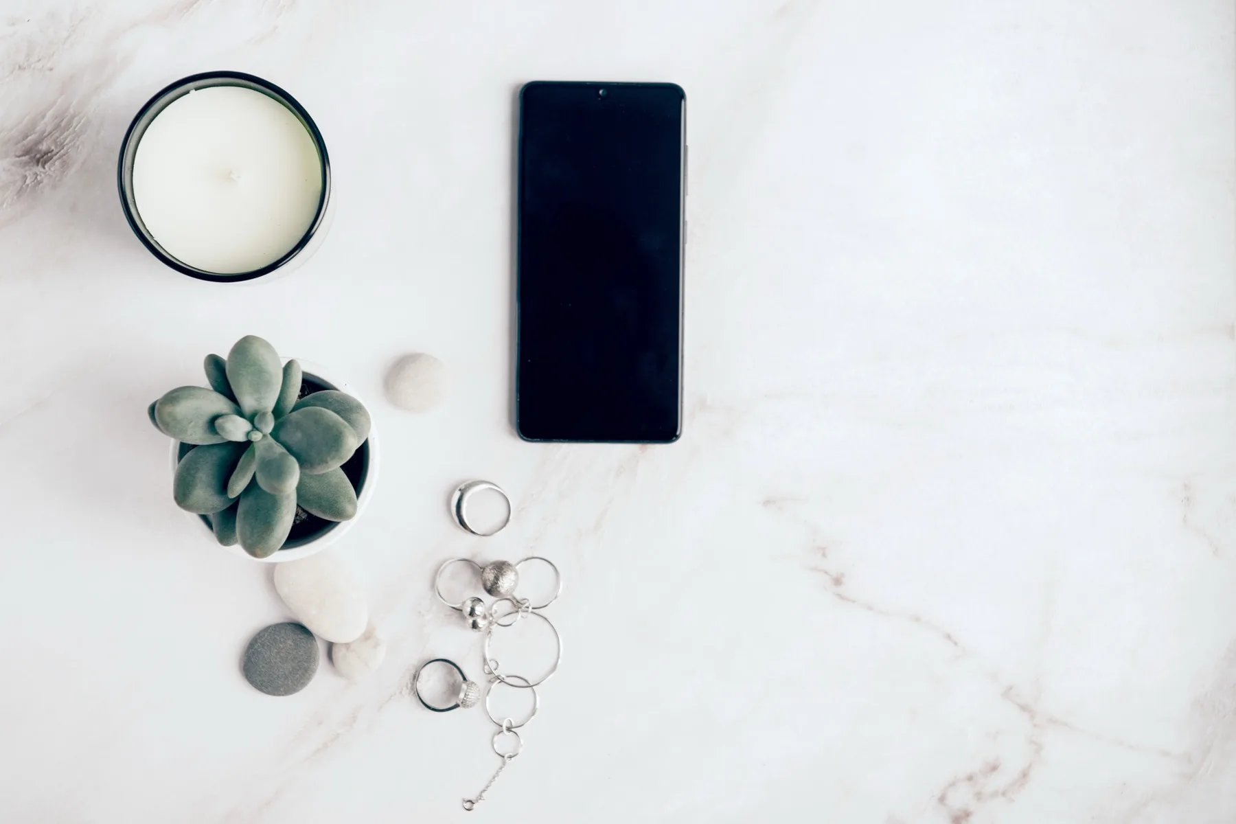 Phone beside a candle, succulent and jewellery on white marble