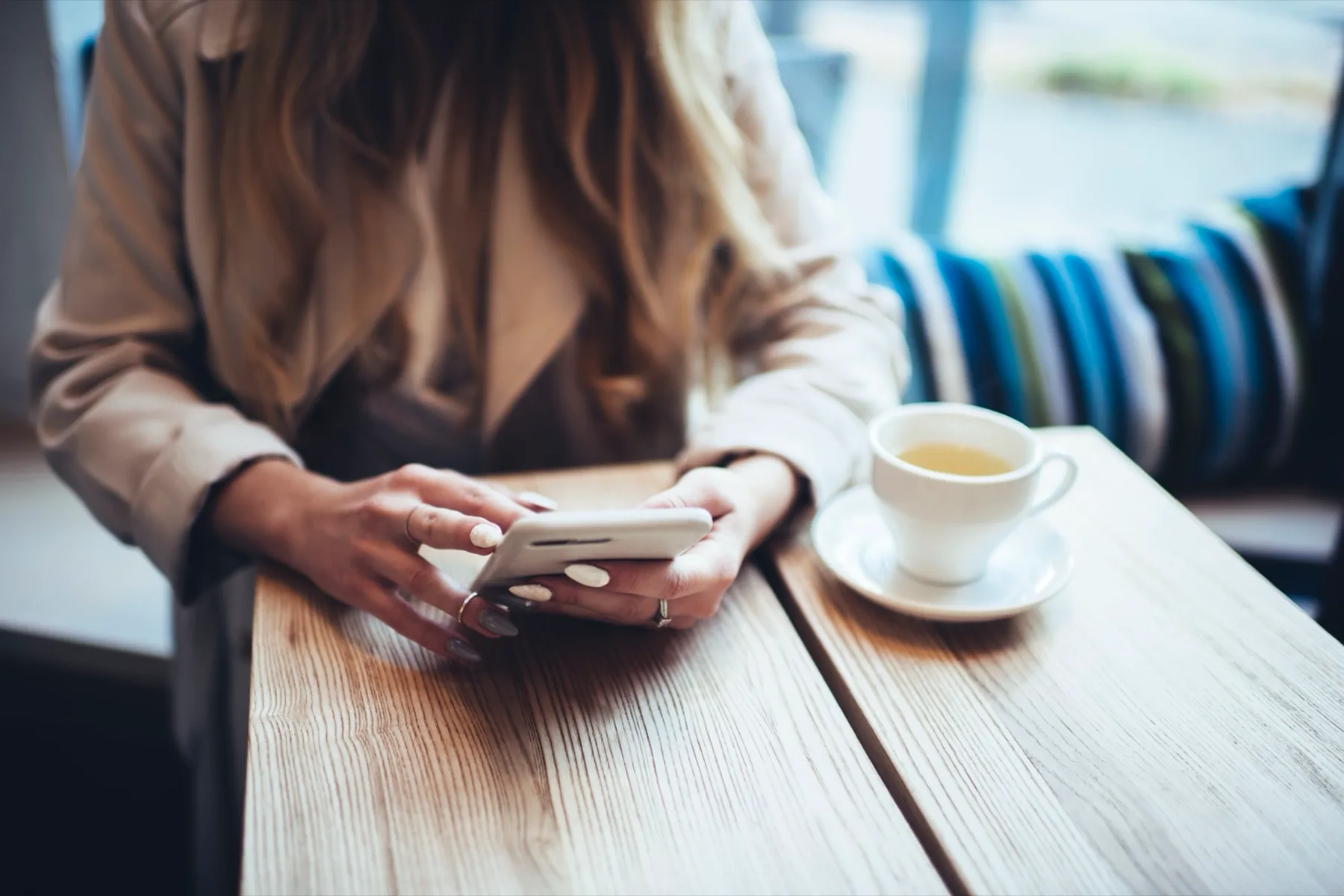 Woman scrolling her phone at a cafe table with a cup of tea