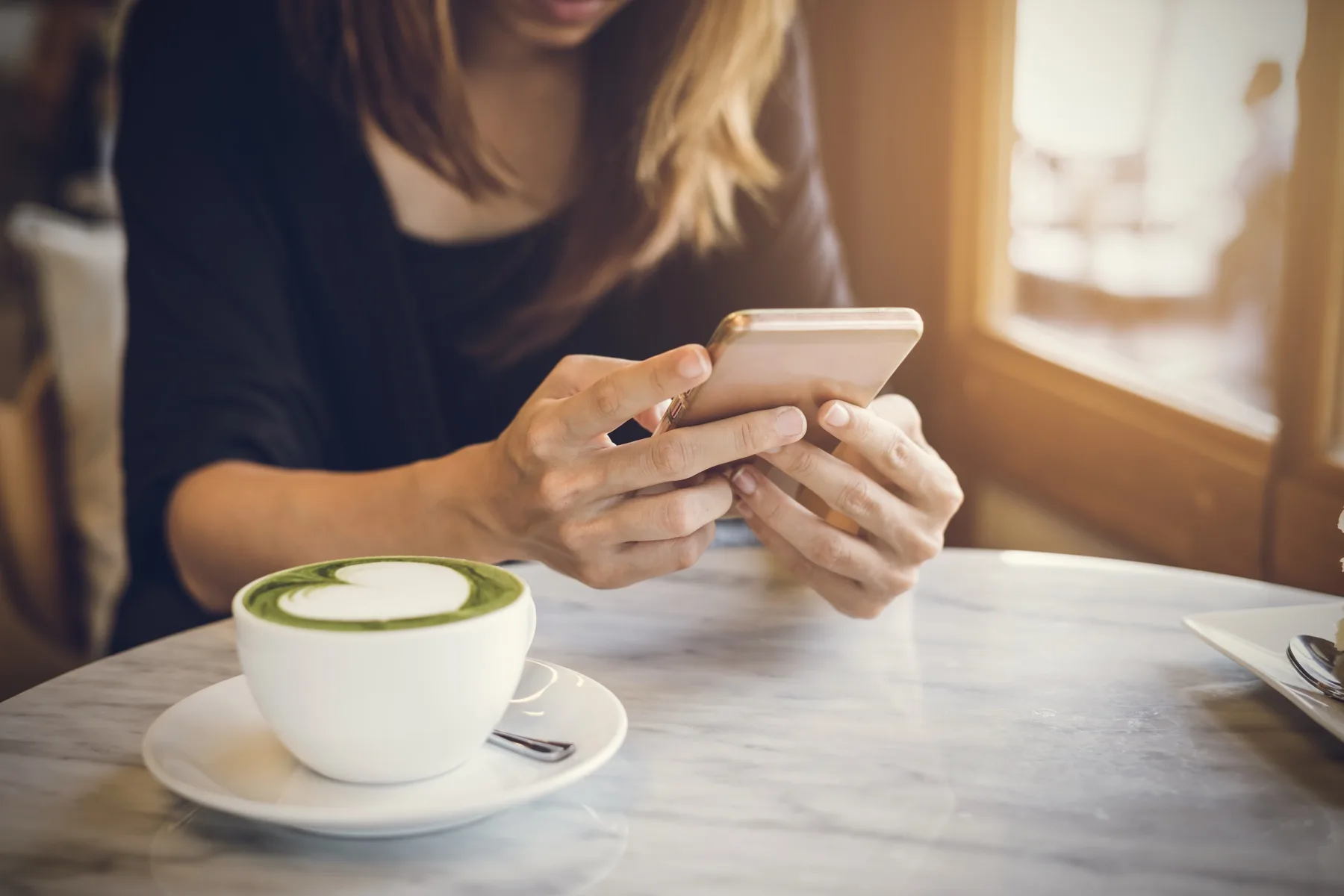 Woman using her phone beside a matcha latte