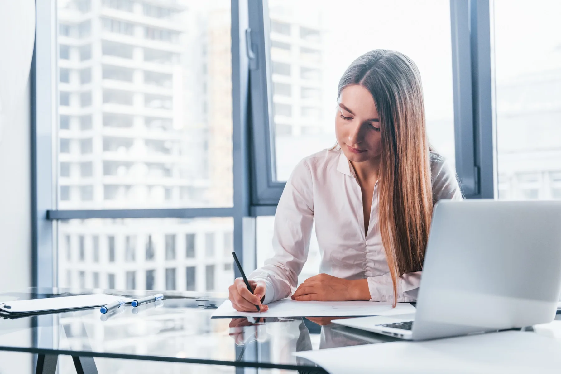 Woman writing notes beside her laptop in a modern office