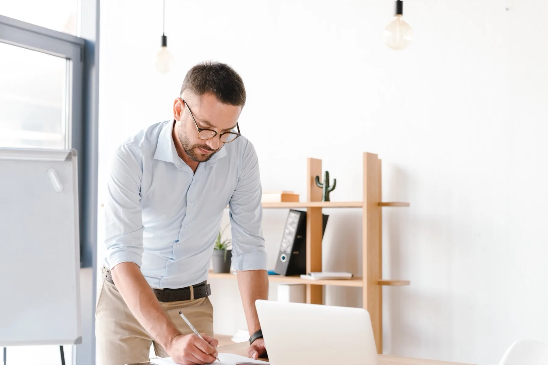 Man standing at his desk writing notes next to a laptop