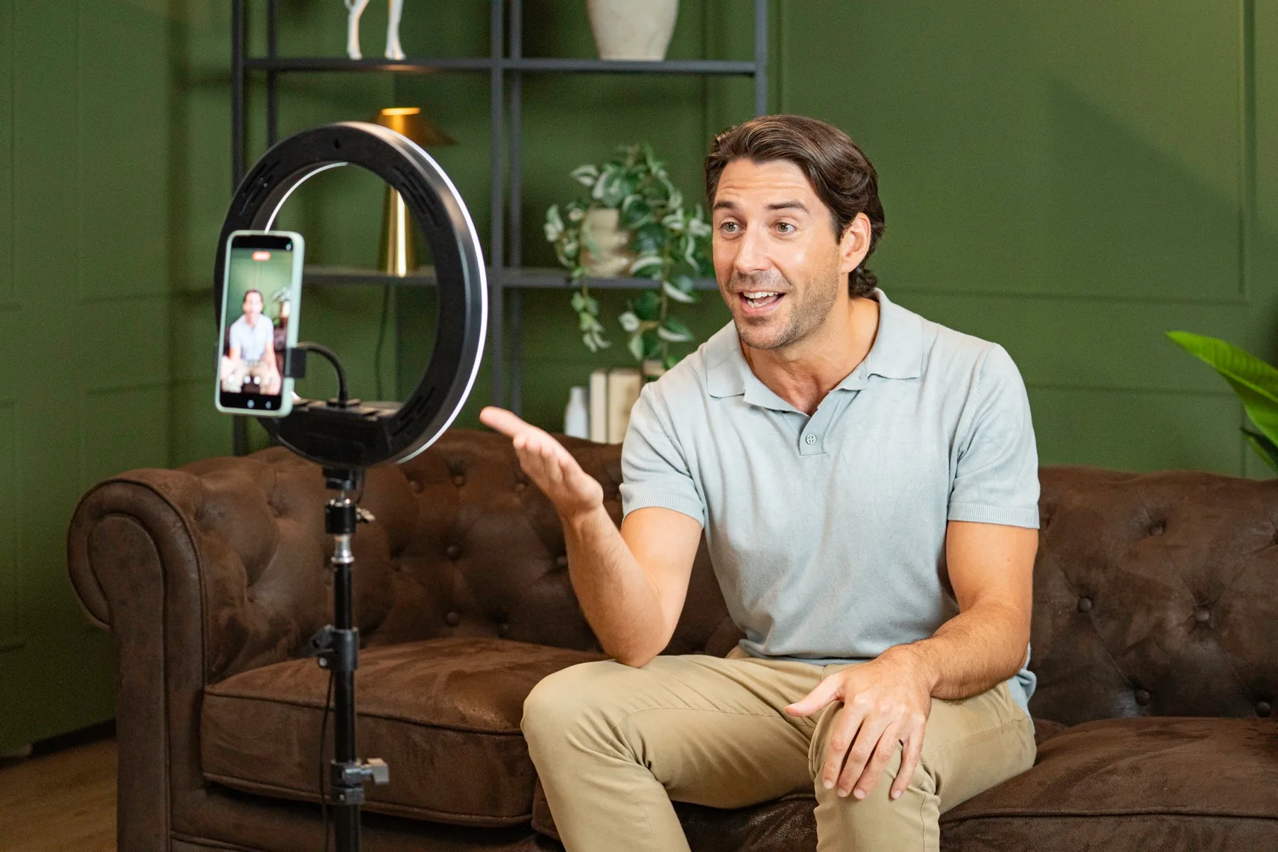 Man on a sofa talking to camera while recording on a phone and ring light
