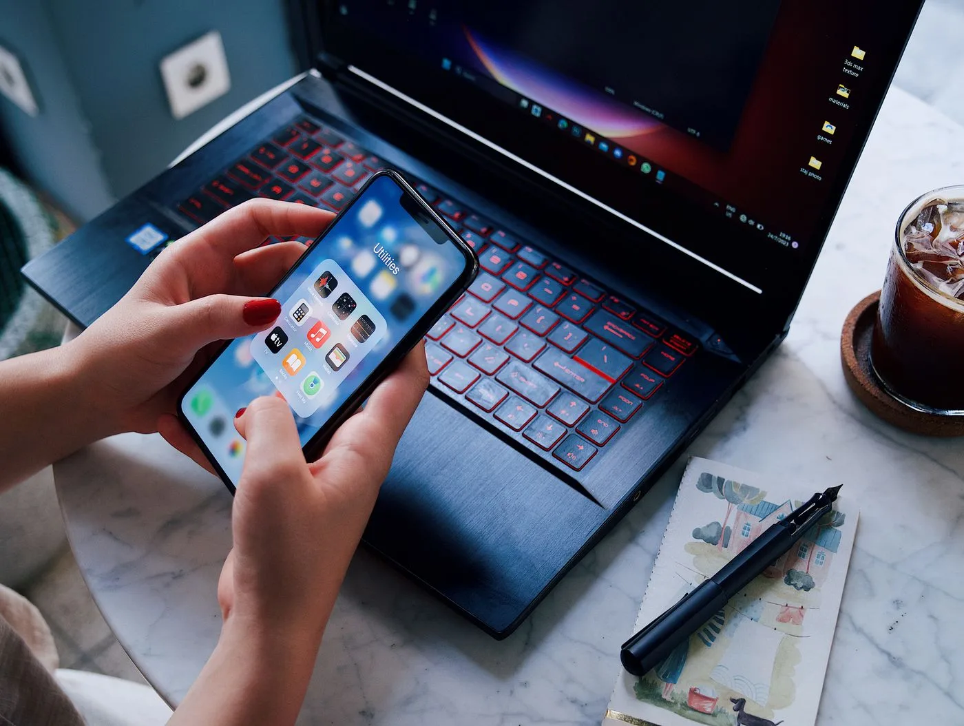 Hands holding a smartphone over a laptop with iced drink. Modern technology in everyday life